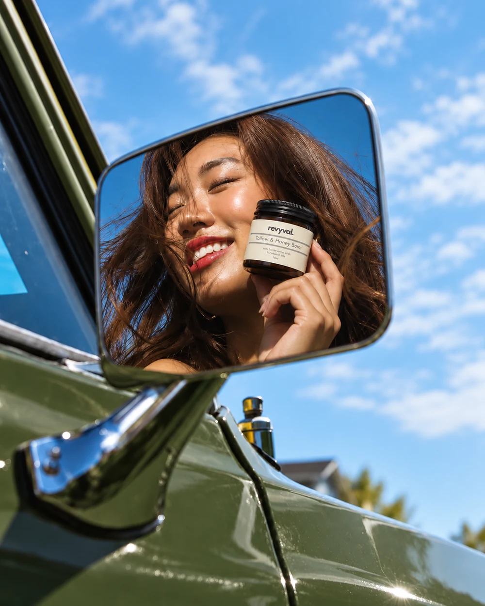 A woman smiling in a car mirror while holding her Revyval balm